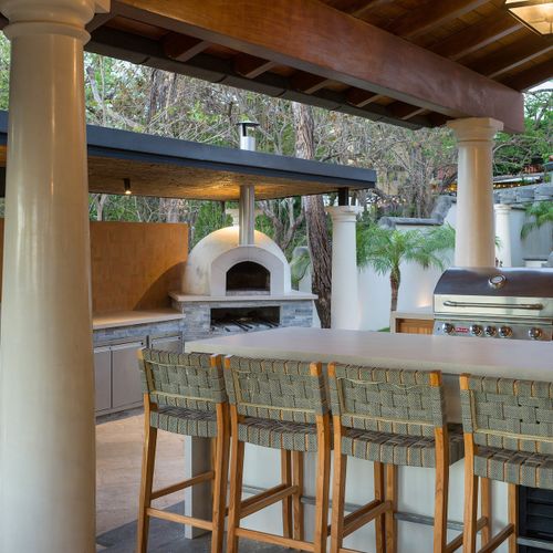 Outdoor bar - bar stools facing a wood-fired pizza oven and stainless gas BBQ. Dinner, social.