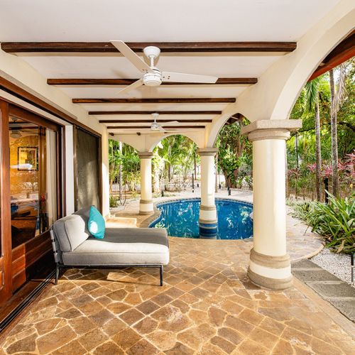 Arched colonnade veranda - exposed beams, ceiling fans, chaise tucked beside the pool.