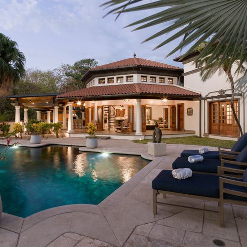 Twilight pool view of Casa Libelula Mediterranean estate with terracotta turret roofline and lit interiors, Playa Langosta, Tamarindo.