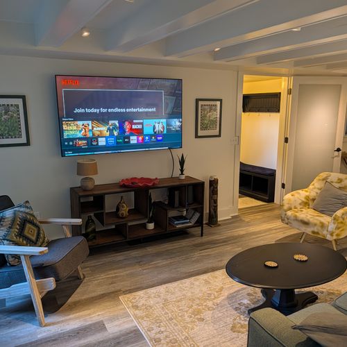LIVING ROOM (FIRST FLOOR):  The home has a beautiful living room with a sofa, chairs, coffee table, lamps, and a large screen television.