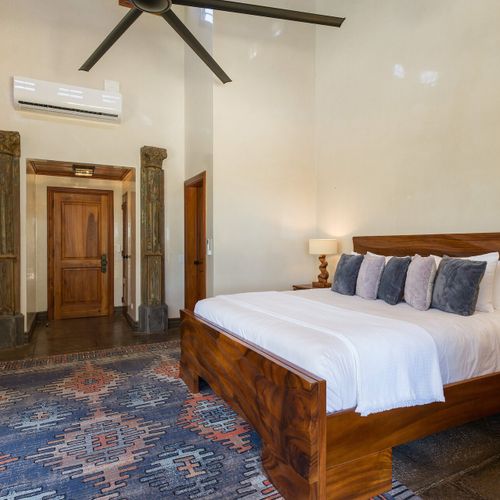 Master king suite - vaulted ceiling, antique carved column doorway, walnut bedframe, Persian-style rug.