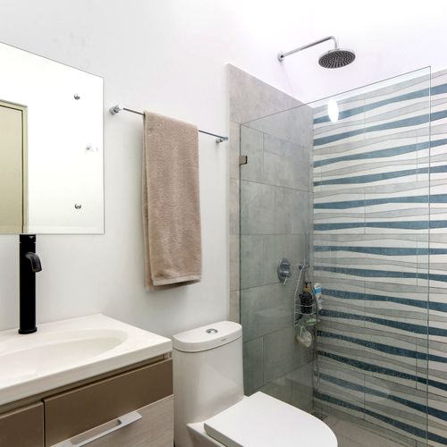 Full bathroom featuring a glass walk-in shower with blue wave-pattern tile, floating vanity, and rain showerhead, in Casa Margarita, Tamarindo, Costa Rica.