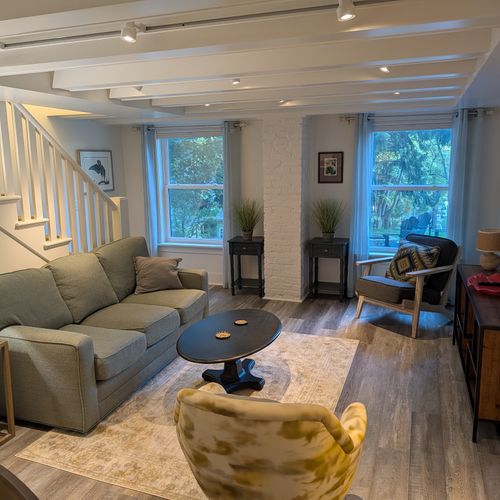 LIVING ROOM (FIRST FLOOR):  The home has a beautiful living room with a sofa, chairs, coffee table, lamps, and a large screen television.