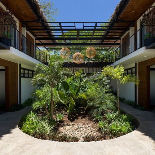 Open-air interior tropical courtyard with circular planted garden and woven rattan pendant lights between villa wings at Casa Oso, Tamarindo, Costa Rica