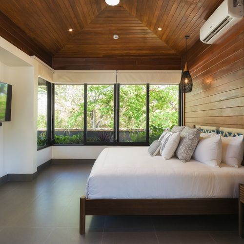 Luxury king bedroom with full hardwood walls and ceiling, vaulted roofline and wraparound jungle-view windows at Casa Oso luxury villa, Tamarindo.