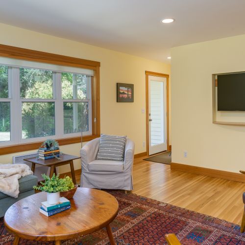 Relax in the comfortable living room with a smart TV, cozy seating, and large windows that bring in natural light and peaceful garden views.