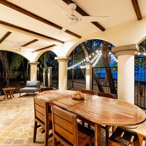 Beachside covered terrace at twilight - Edison string lights, arched openings, Tamarindo Bay just past the gate.