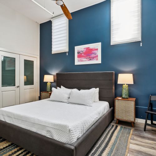 Moody blue bedroom w/ bed & warm bedside lighting.