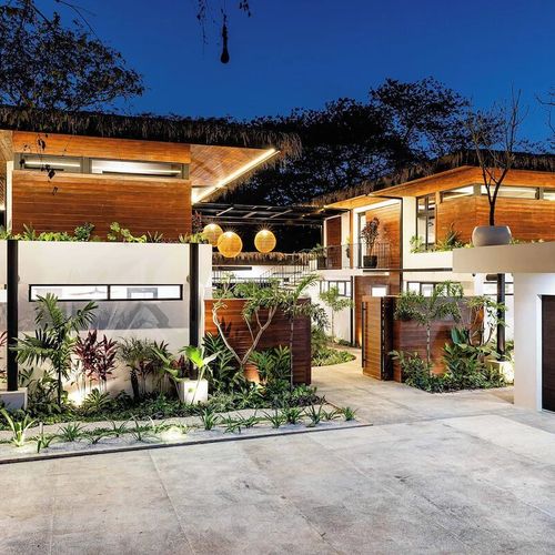 Modern tropical architecture in wood and white, framed by palapa roofs and lush landscaping — your private arrival each evening.