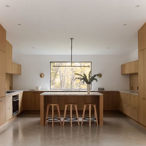 Chef's kitchen in white oak with a stone island, counter seating, and a forest view.