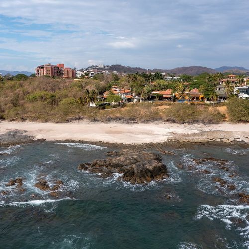 Aerial of Playa Langosta - white-sand beach, dramatic rocky points, Tamarindo town just up the coast.