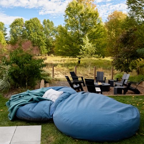 Oversized loungers on the pool deck with propane fire pit in the background and meadow beyond.