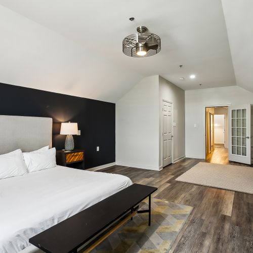 Moody bedroom w/ dark accent wall, bed & wood floors.