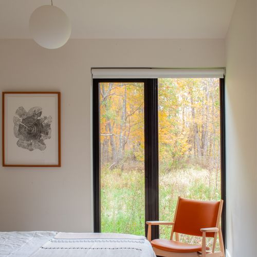 Serene bedroom with a leather lounge chair framing the meadow beyond.