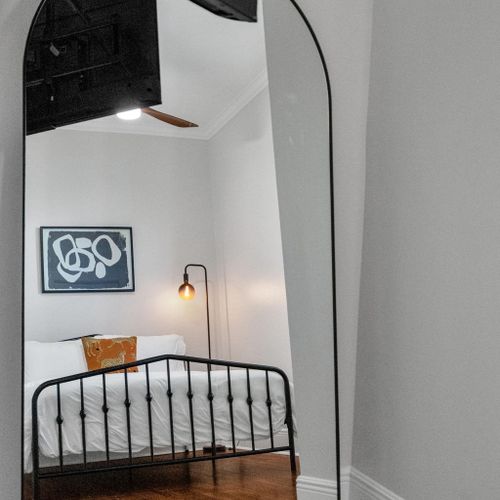 Unwind in this inviting bedroom w/ warm lamp light, bold artwork & a classic iron bed