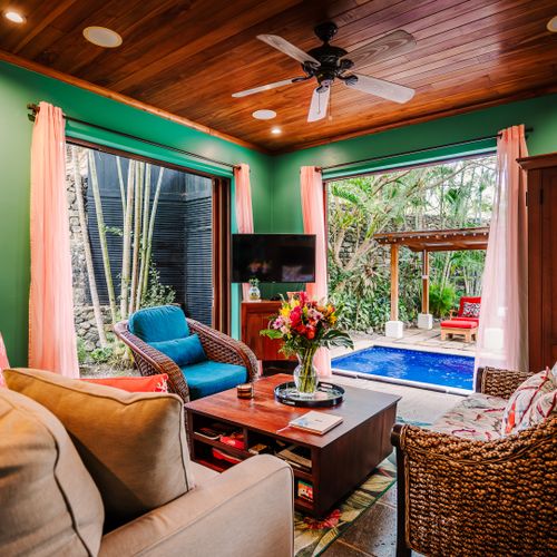 Elegant indoor lounge with comfortable sofas, TV, fine art decor, and coastal style at this exclusive villas Tamarindo. Large windows frame the pool and tropical garden outside, creating seamless indoor-outdoor living for your getaway in Langosta.
