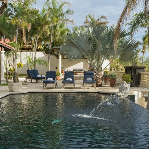 Resort-style pool with chaise loungers, fountain feature and palm-lined deck.
