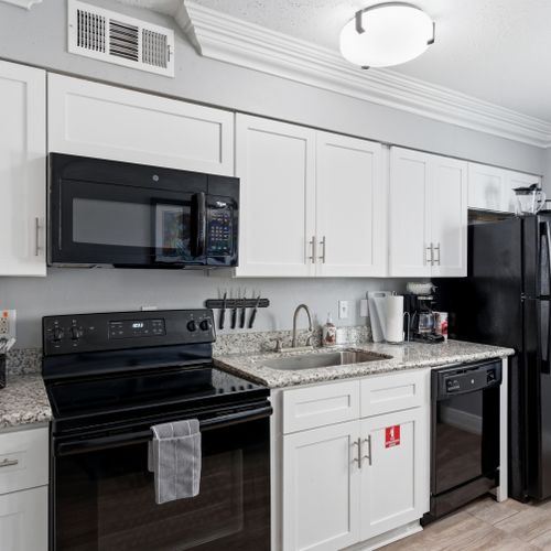 Unit 203 modern kitchen w/ crisp white cabinetry & black appliances.