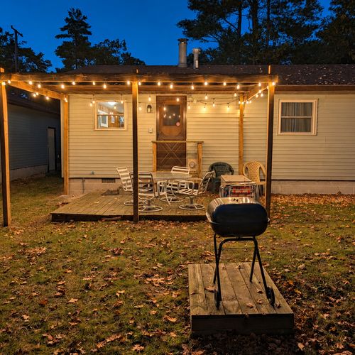 OVERVIEW:  The back of the cottage at night, highlighting the charcoal grill, the backyard deck, and the outdoor furniture.
