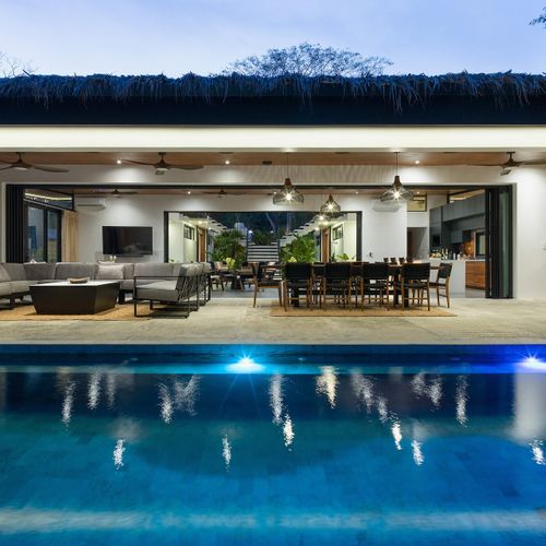 Covered poolside lounge terrace with two large sectionals and ceiling fans, overlooking an infinity pool and tropical jungle at Casa Oso, Tamarindo.