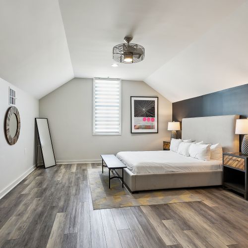 Vaulted-ceiling bedroom w/ bed & warm wood floors.