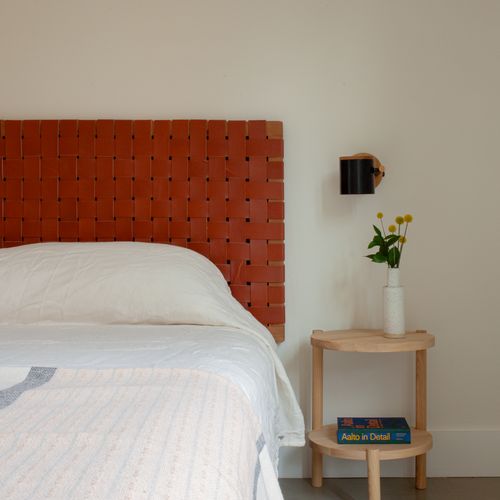 Restful primary bedroom with a woven leather headboard and curated design books.