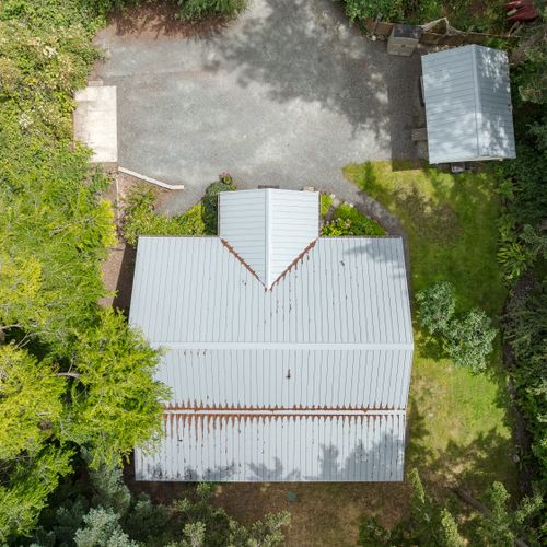 A bird's-eye view of the property showcases the spacious yard, private driveway, and peaceful surroundings tucked beneath a canopy of mature trees.