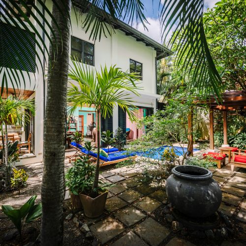 Tropical garden view featuring pool, cozy bungalow, and beautifully designed house in background at this Langosta luxury vacation rental. Exquisite decor, coastal style, fine art touches, and lush nature for an elegant beach retreat.