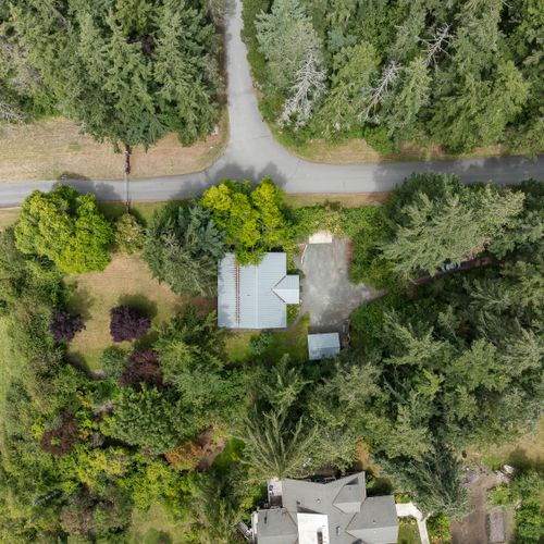 A bird's-eye view of the property showcases the spacious yard, private driveway, and peaceful setting surrounded by mature trees.