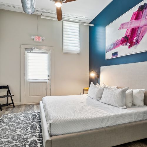 Bright bedroom w/ bed, colorful art & direct door access outside.