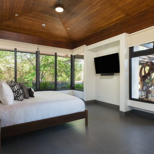 Luxury king bedroom with vaulted wood ceiling and wraparound jungle-view windows at Casa Oso luxury villa, Tamarindo, Costa Rica.