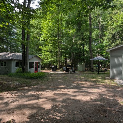 EXTERIOR: The full backside view of the property from the secondary driveway. The wonderful cabin is on the left, the gorgeous firepit and grill and the cute metal picnic table are in the middle, on the right is the garage not for guest use