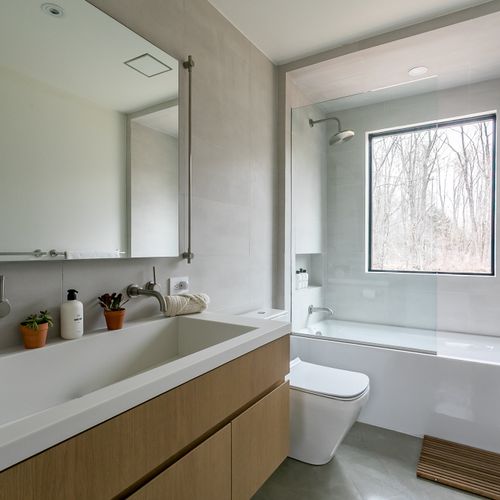 A clean, spa-like bath with a floating oak vanity, deep soaking tub, and a window framing the outdoors