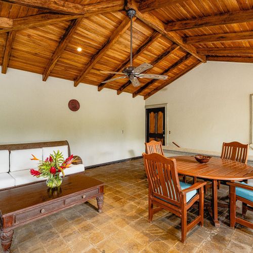 Covered open-air lanai — vaulted hardwood ceiling, four-top dining and a wicker sectional facing the canopy.
