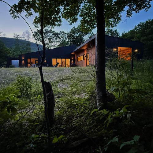 As evening falls, The Heron House glows against the meadow and the Catskills beyond.