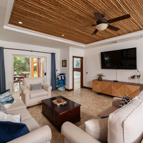 Modern beach decor living room with flat-screen TV, bright natural light, and coastal style at luxury Playa Langosta condo, Tamarindo, Costa Rica. Open space, comfortable seating, and vacation rental amenities near surf and restaurants.