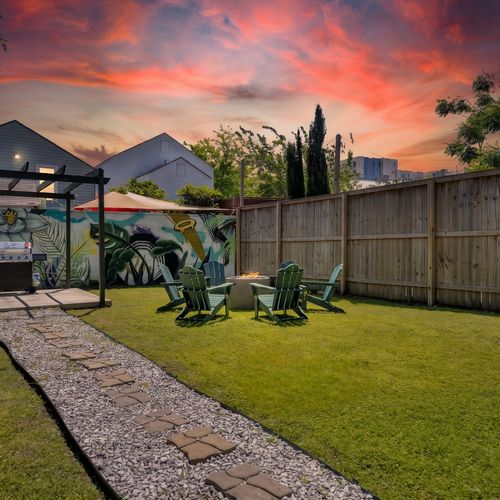 Spacious yard w/ green grass, Adirondack chairs, firepit & a vibrant mural backdrop.