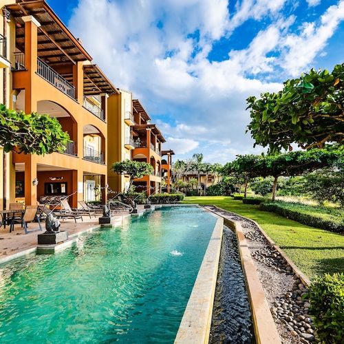 Beachfront pool with tropical garden and contemporary building design at luxury Playa Langosta condo, Tamarindo, Costa Rica. Palm trees, lounge area, sun loungers, and direct beach access. Steps from surf, restaurants, and vacation rentals.