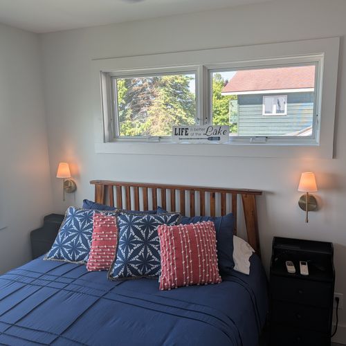 BEDROOM #1 (SECOND FLOOR):  Features a queen-size bed, nightstands, lamps, ceiling fan, mini-split A/C unit, television, dresser, closet, mirror, and a great view of Crystal Lake!