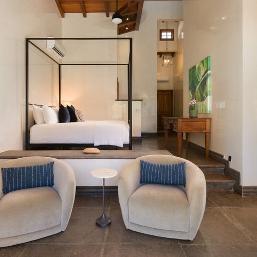 Four-poster king ensuite from the seating area - curved velvet armchairs, antique carved doors.