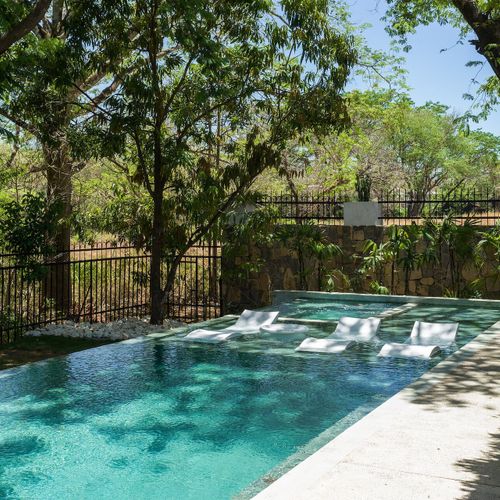 Private infinity pool with floating sun loungers and tropical jungle view at Casa Oso luxury villa, Tamarindo, Costa Rica.