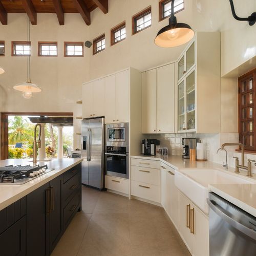 Chef's kitchen with vaulted exposed-beam ceiling, navy quartz island, glass-front cabinets and clerestory windows ringing the room.