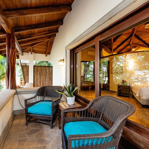 Master suite private balcony — wicker chairs in the canopy, sliding doors back to the king bedroom.