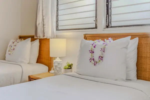 Comfortable bed setup featuring plush pillows, a nightstand lamp, and a window. 🛏️