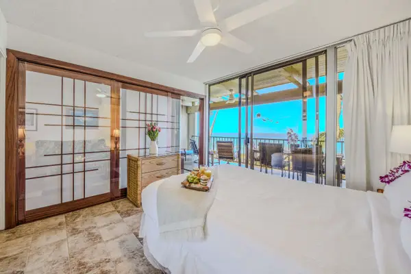 Comfortable bed setup featuring a cooling ceiling fan and a beautiful ocean view. 🛏️