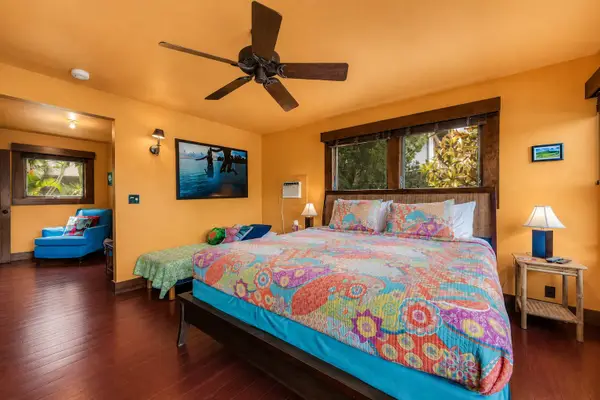 Warm bedroom presents colorful bedding, bedside tables, and tropical artwork