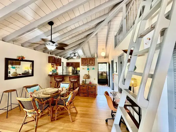 Living room view highlights table, rattan chairs, artwork, and ladder