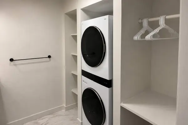 This modern utility area features a stacked washer/dryer integrated into custom white shelving.