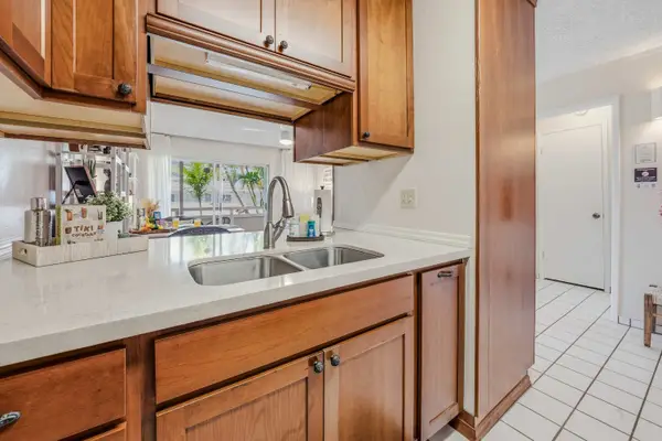 Kitchen setup with double stainless steel sink, wooden cabinets & white countertops