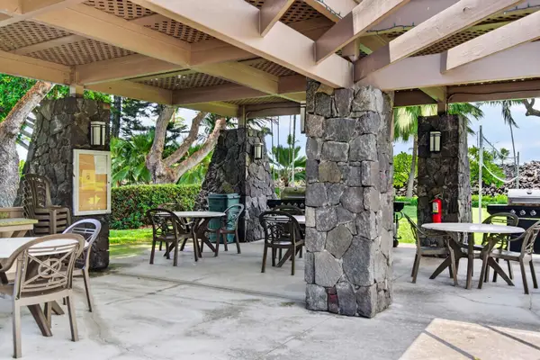 Outdoor covered pavilion with stone pillars, dining tables, and BBQ grills